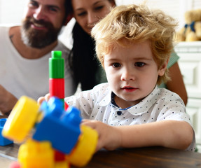 Parents watch their son with busy face making brick constructions