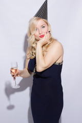 Beautiful young blond woman at the party. The girl is dressed in evening dress with a festive cap, in her hand holds a glass of champagne.