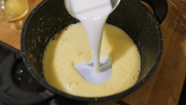 Mixing milk with eggs and whipping it in pot.