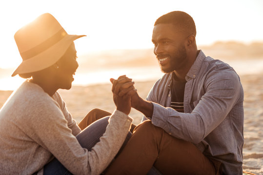 Young African couple sitting together on a beach at sunset - Powered by Adobe