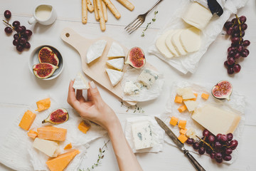 Various types of cheese with fruits and snacks on the wooden white table. Top view