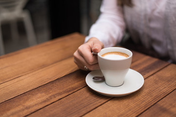Woman's hand holding coffee cup on wooden table.