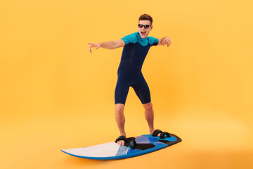 Image of happy surfer in wetsuit and sunglasses using surfboard