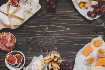 Cheese selection with fruits and snacks on the wooden dark table with copy space. Top view background