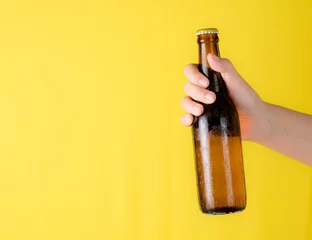 Draagtas Hand holding beer bottle with text space against yellow background © showcake