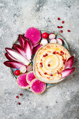 Homemade hummus seasoned with olive oil and paprika and fresh vegetables: radishes, watermelon radish, red chicory, pomegranate. Healthy vegetarian appetizer or snack platter