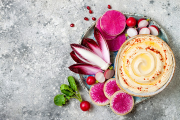 Homemade hummus seasoned with olive oil and paprika and fresh vegetables: radishes, watermelon radish, red chicory, pomegranate. Healthy vegetarian appetizer or snack platter