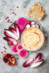 Homemade hummus seasoned with olive oil and paprika and fresh vegetables: radishes, watermelon radish, red chicory, pomegranate. Healthy vegetarian appetizer or snack platter