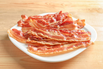 Plate with cooked bacon rashers on wooden table