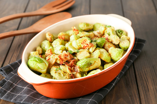 Casserole with Brussels sprouts and bacon on wooden table