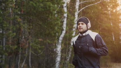 Handsome runner man in headphones jogging while listening music in winter park in the morning