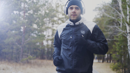 Fototapeta premium Attractive runner man in headphones jogging while listening music in winter park in the morning