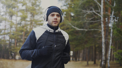 Handsome runner man in headphones jogging while listening music in winter park in the morning