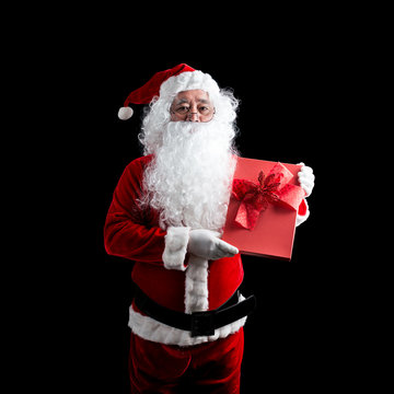 Photo of happy Santa Claus with red gift box of Christmas present in hands, isolated on black background.