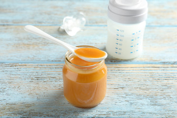 Jar and spoon with healthy baby food on wooden table