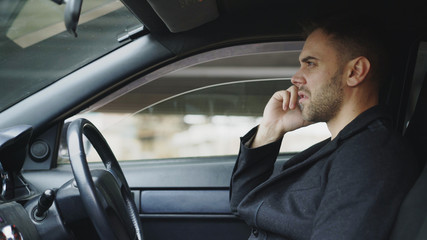 Stressed businessman swearing and talking phone while sitting inside car outdoors