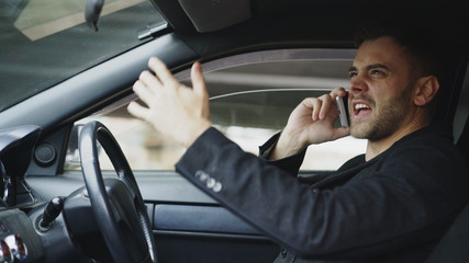 Stressed businessman swearing and talking phone while sitting inside car outdoors