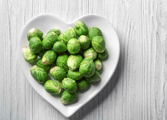 Heart-shaped plate with raw fresh Brussels sprouts on wooden background