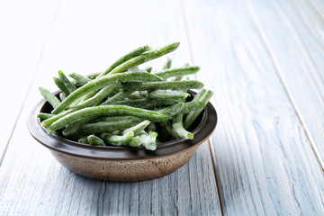 Bowl with frozen green beans on wooden background