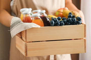 Woman holding wooden crate with delicious juices in bottles and ingredients