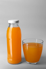 Bottle and glass with juice on light background