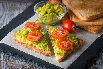 Avocado toast, cherry tomato on wooden background. Breakfast with toast avocado, vegetarian food, healthy diet concept.