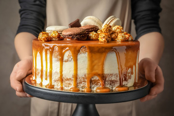 Woman holding stand with delicious caramel cake