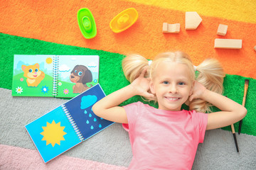 Cute little girl with toys on color carpet in kindergarten