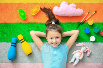 Cute little girl with toys on color carpet in kindergarten
