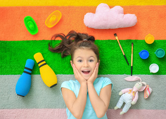 Cute little girl with toys on color carpet in kindergarten