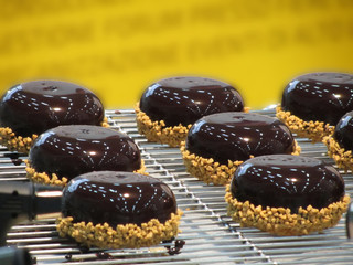 Small glazed chocolate cakes with hazelnut grains on yellow background