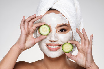 Attractive smiling lady with scrab on face holding cucumber slices isolated