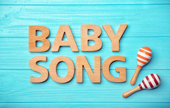 Text BABY SONG and toy maracas on wooden background