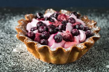 Fresh fruit and berry tart dessert with toss sugar on wooden background. Delicious sweet cake with raspberries, figs, strawberries, cherry, and cream.