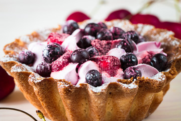 Fresh fruit and berry tart dessert with toss sugar on wooden background. Delicious sweet cake with raspberries, figs, strawberries, cherry, and cream.