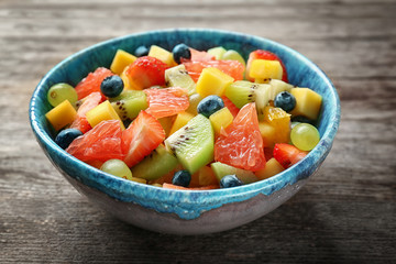 Bowl with delicious fruit salad on wooden background