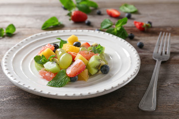 Plate with delicious fruit salad on table