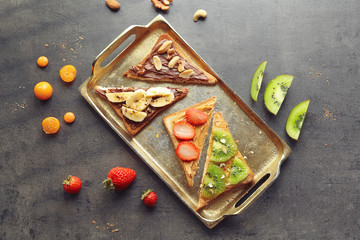Delicious toasts with chocolate paste, peanut butter and fruits on metal tray