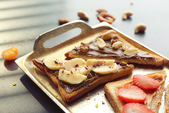 Delicious toasts with chocolate paste, fruits and nuts on metal tray