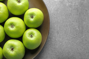 Plate with fresh green apples on grey background