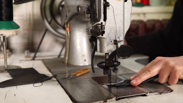 Close up shot of skilled leathersmith working on a sewing machine in a workshop. He is sewing leather stripes together.
