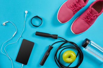 Flat lay shot of Sport equipment. Sneakers, jump rope, earphones and phone on blue background.
