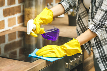 Woman in the kitchen wiping dust using a spray and a duster while cleaning her house, close-up
