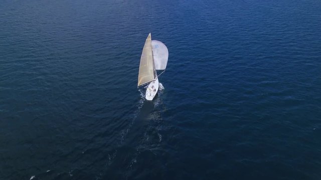 top view from high in sky of aerial drone flying over beautiful speed yacht or competition professional sailboat, team of sailors sets up spinnaker sail, amazing open water views