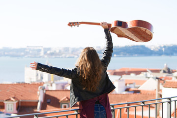 Cheerful Girl Holding Guitar Above Head on Rooftop