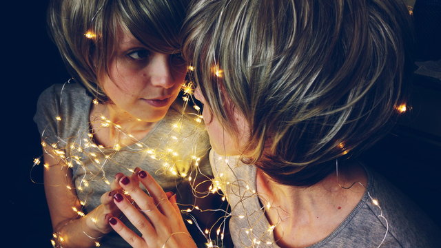 Fototapeta Mujer joven rodeada de luces de navidad reflejándose en un espejo 