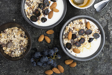 Breakfast from healthy seasonal ingredients: granola, flakes, honey, dark grapes, almonds in a...