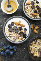 Breakfast from healthy seasonal ingredients: granola, flakes, honey, dark grapes, almonds in a serving gray pial on a gray grunge background. Top view. Vegetarian Organic Food Concept.