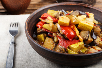 Vegetable stew with tomato, eggplant, zucchini, onion, carrot, pepper, close-up on a clay plate.