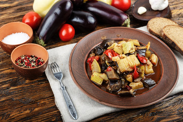 Vegetable stew with tomato, eggplant, zucchini, onion, carrot, pepper, close-up on a clay plate.